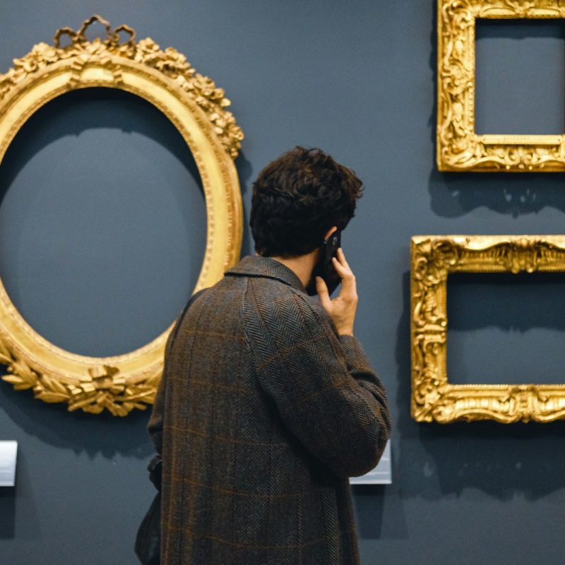 man in black jacket standing in front of brown wooden frames